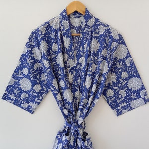 Op de afbeelding: Een blauwe en witte bloemenprint badjas met een witte bies. De badjas heeft een ceintuur en driekwart mouwen.
