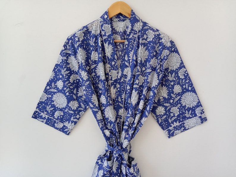 Op de afbeelding: Een blauwe en witte bloemenprint badjas met een witte bies. De badjas heeft een ceintuur en driekwart mouwen.