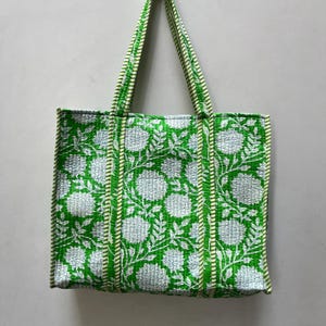 May include: A green and white tote bag with a floral print. The bag has two long straps and is made of a quilted fabric.