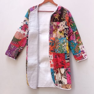 May include: A long, open patchwork jacket with a vibrant mix of floral and geometric patterns in red, pink, purple, and blue. The jacket has a white lining and trim, and is displayed on a wooden hanger.