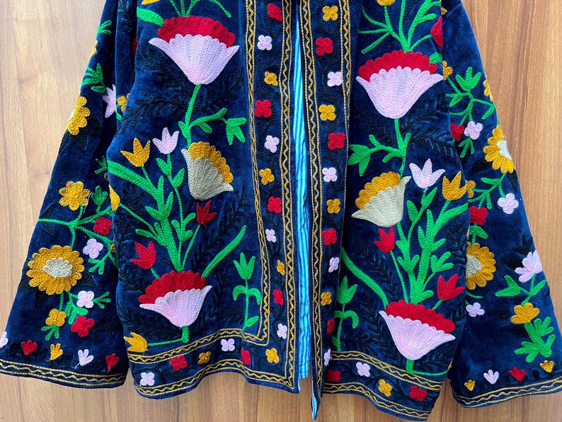 May include: A dark blue embroidered jacket with a floral design. The jacket features red, pink, yellow, and white flowers with green leaves. The edges are trimmed with gold and red embroidery.