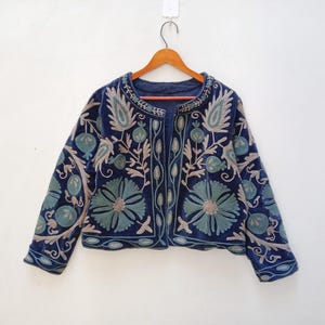 May include: A navy blue velvet jacket with intricate floral embroidery in shades of green and beige. The jacket has a round neckline and a front closure.