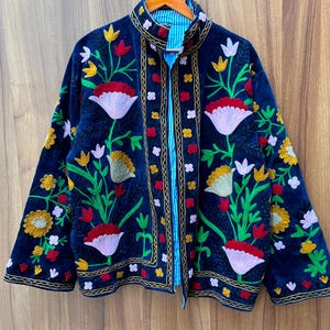 May include: A dark blue velvet jacket with colorful floral embroidery. The jacket features a mandarin collar and a striped blue lining. The embroidery includes red, yellow, white, and pink flowers with green leaves.