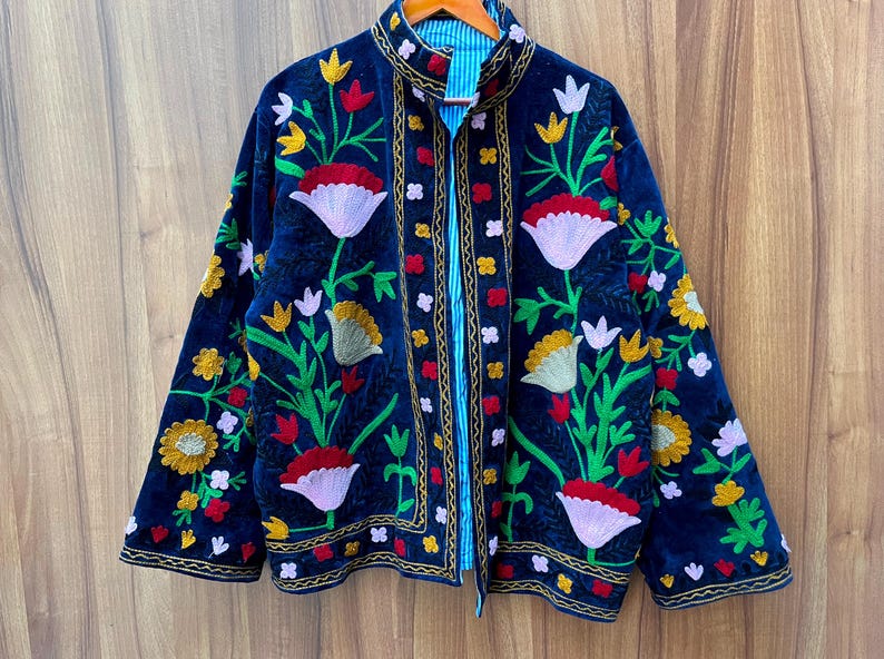 May include: A dark blue velvet jacket with colorful floral embroidery. The jacket features a mandarin collar and a striped blue lining. The embroidery includes red, yellow, white, and pink flowers with green leaves.
