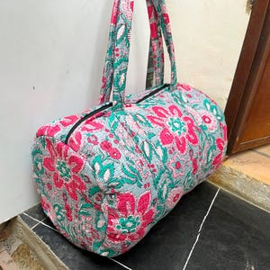 Könnte beinhalten: Eine Reisetasche mit floralem Muster auf hellblauem Grund und rosa und grünen Blumen. Die Tasche hat zwei schwarze Henkel.