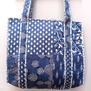 Peut inclure: Un sac fourre-tout bleu et blanc en patchwork avec un motif matelassé. Le sac a deux longues anses et est fait de tissu en coton.