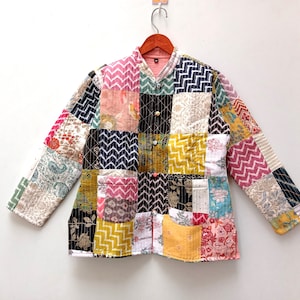 Può includere: Una giacca trapuntata patchwork con una varietà di motivi floreali e geometrici in tonalità di rosa, blu, verde, giallo e marrone. La giacca ha un colletto alla coreana e una chiusura con bottoni.