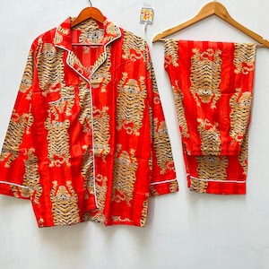 Puede incluir: Conjunto de pijama rojo y blanco con estampado de tigre. La parte superior tiene mangas largas y un cierre de botones en la parte delantera. Los pantalones tienen una cintura elástica.