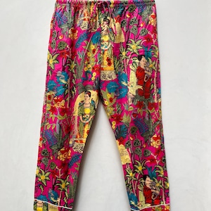 Könnte beinhalten: Rosa Schlafanzughose mit einem bunten Blumenmuster mit mehreren Bildern von Frida Kahlo. Die Hose hat einen Kordelzugbund und weiße Paspeln an den Säumen.