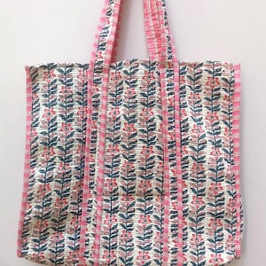 May include: A white tote bag with pink and blue floral print. The bag has pink and white striped straps.