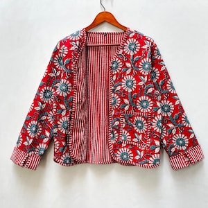May include: Red quilted jacket with a floral print in blue and white. The jacket has a striped lining and a pocket on the left side.