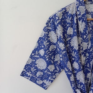 Op de afbeelding: Een blauwe en witte bloemenprint badjas met een witte bies. De badjas heeft een lange mouw en een strikceintuur.
