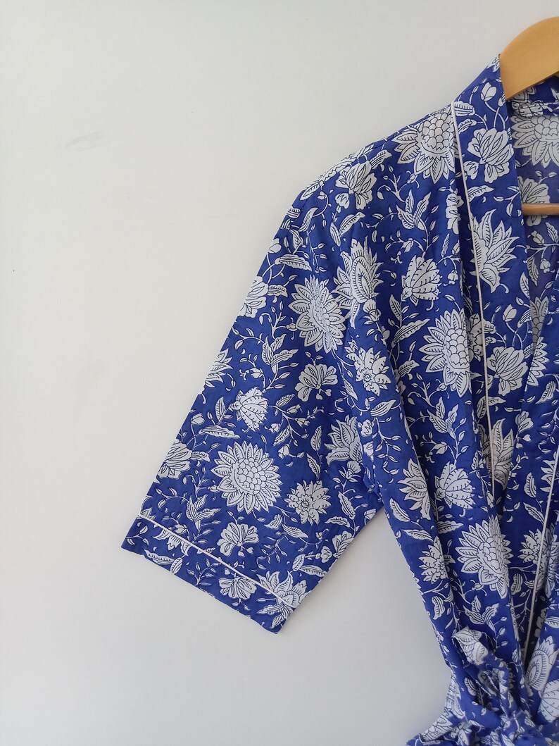 Op de afbeelding: Een blauwe en witte bloemenprint badjas met een witte bies. De badjas heeft een lange mouw en een strikceintuur.
