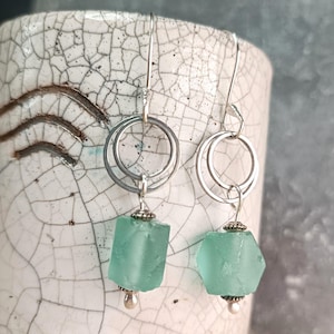 Könnte beinhalten: Silberne Hängeohrringe mit geometrischen, mintgrünen Perlen. Jeder Ohrring hat ein Doppelreifen-Design. Die Perlen sind strukturiert und an einer dekorativen Silberkappe und einer kleinen Silberperle aufgehängt.