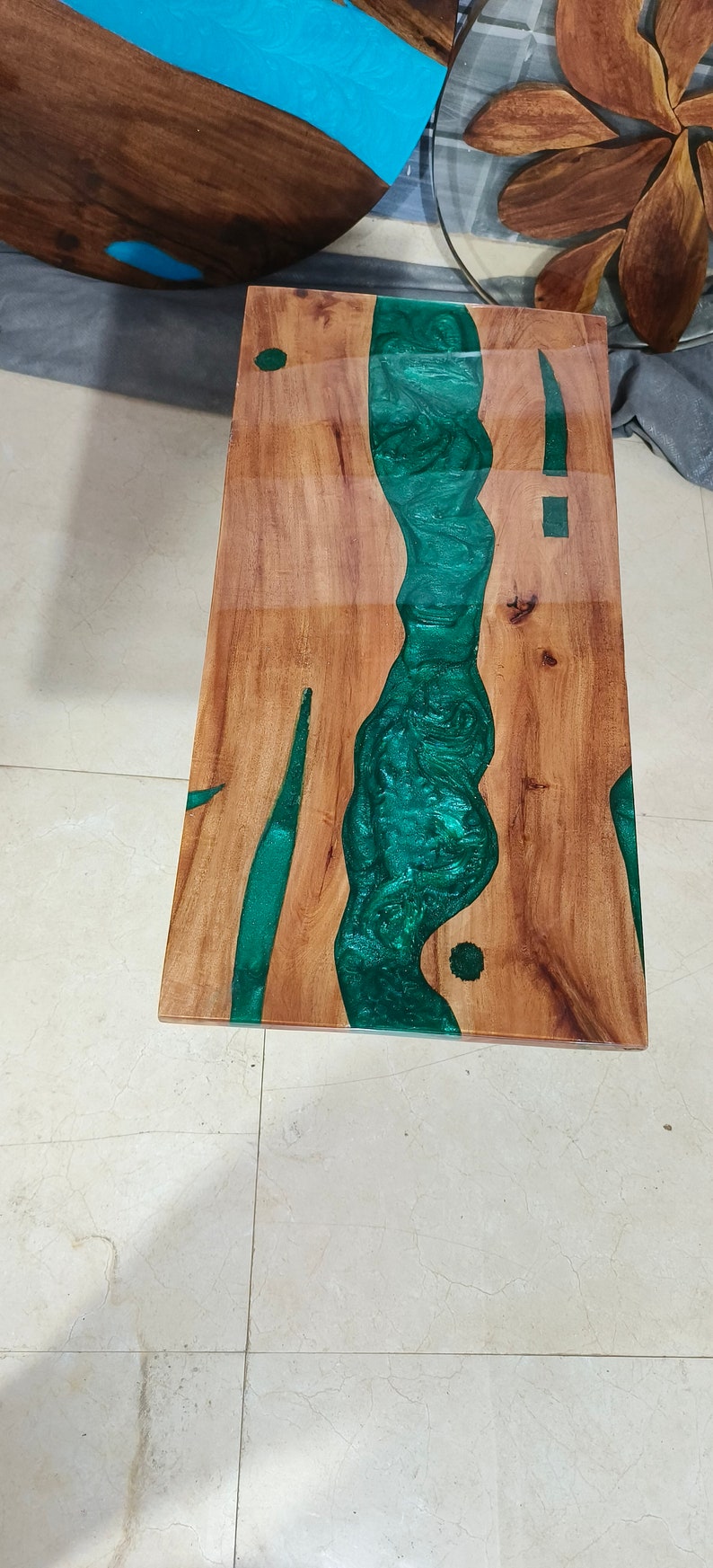 May include: A rectangular wooden table with a river of green epoxy resin running through the center. The wood has a natural grain, and the resin has a glossy finish. The table is a unique piece of furniture.