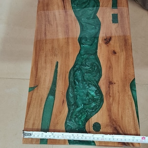 May include: Wooden rectangular table with a river of green epoxy resin. The table is made of light brown wood and the resin flows through the center. The table is approximately 30 inches long.