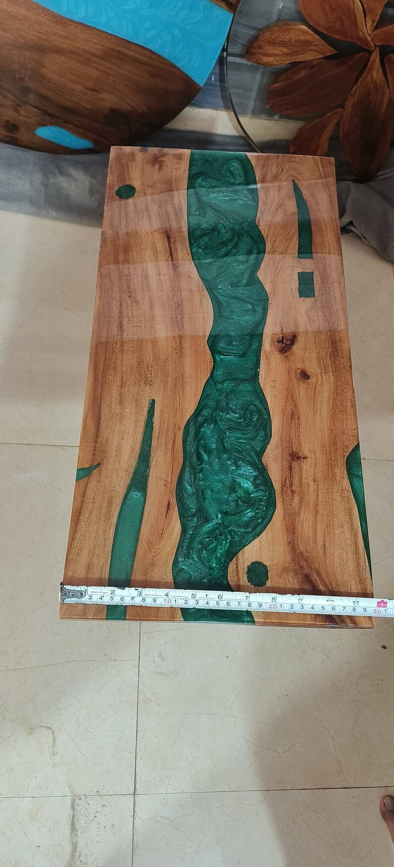 May include: Wooden rectangular table with a river of green epoxy resin. The table is made of light brown wood and the resin flows through the center. The table is approximately 30 inches long.