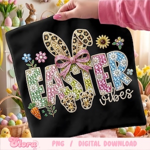 May include: Black graphic tee with the words "EASTER vibes" in a floral design. The design includes bunny ears with a leopard print, a pink bow, and a carrot. The tee is held by a person.