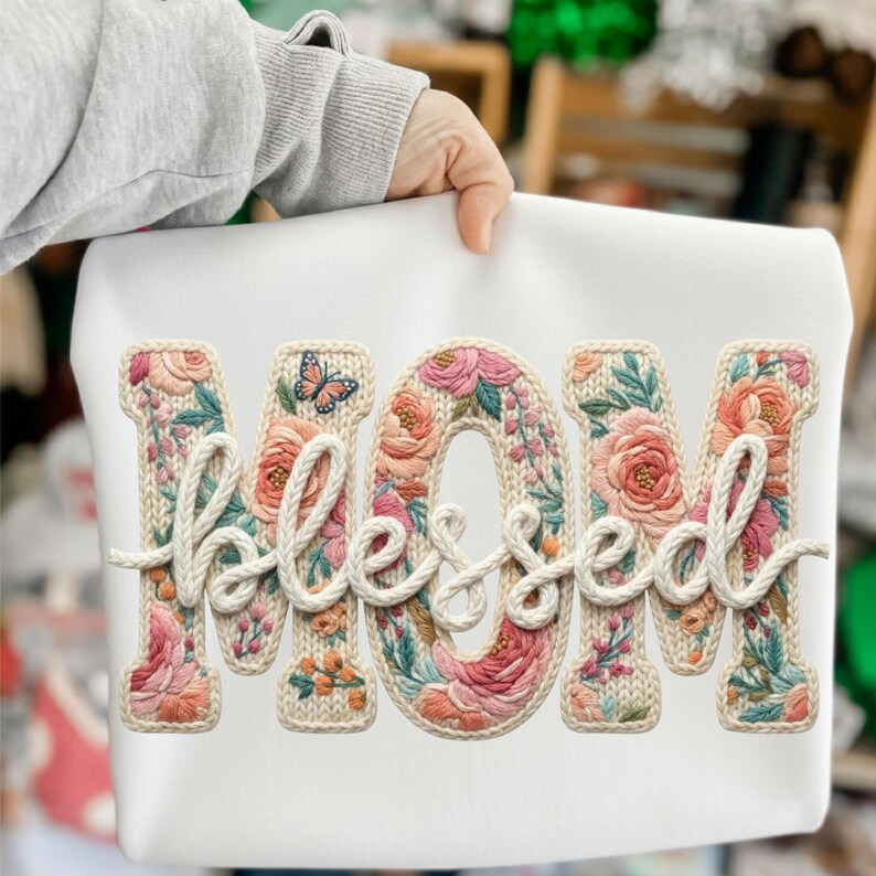 May include: White sweatshirt with the word "MOM" and the word "Blessed" in a floral embroidered design. The letters are filled with pink, peach, and green flowers. A butterfly is embroidered above the "O" in "MOM".