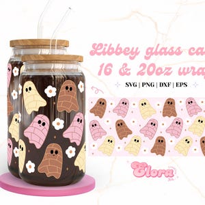 Op de afbeelding: Twee glazen potten met bruine deksels en rietjes, versierd met een patroon van roze en bruine geesten en witte bloemen. De potten zijn gevuld met een donkere vloeistof. De tekst "Libbey glass can 16 & 20oz wrap SVG | PNG | DXF | EPS" staat bovenaan de afbeelding. De tekst "Glora" staat onderaan de afbeelding.
