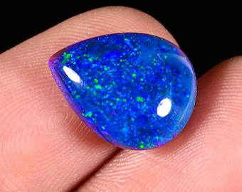 May include: A pear-shaped loose gemstone featuring a deep blue base color with vibrant, scattered flecks of bright green and light blue throughout the surface. The stone has a smooth, polished finish with a reflective sheen and a domed top surface.