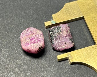 May include: Two pink and black rough cut gemstones. The gemstones are irregular in shape and have a rough, natural finish.