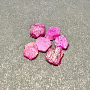 May include: A group of six pink ruby crystals, each with a hexagonal shape and a rough, natural texture.