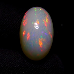 Puede incluir: Una piedra preciosa de ópalo ovalada blanca con destellos iridiscentes de rojo, naranja, verde y azul.