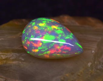 May include: A teardrop-shaped opal gemstone with a translucent white body and a vibrant display of green, red, and orange iridescent flashes.