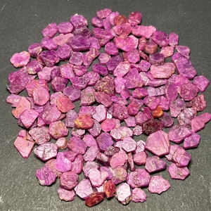 May include: A large pile of pink ruby gemstones. The rough, uncut stones are various sizes and shapes.