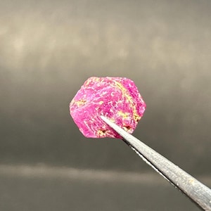 Peut inclure: Gros plan d'un cristal de rubis rose de forme hexagonale. Le cristal est tenu par des pinces.