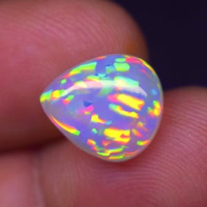 May include: A pear-shaped opal gemstone featuring a translucent white base with vibrant, multi-colored flashes of neon yellow, bright pink, and electric green light reflecting across its smooth, polished, and rounded surface.