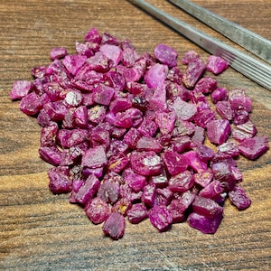 May include: A large pile of loose, raw ruby gemstones. The rubies are a deep, rich red colour and have a variety of shapes and sizes.