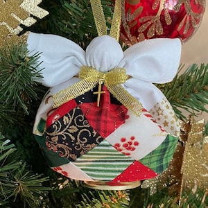 May include: A handmade patchwork angel ornament with a gold ribbon and a small gold cross. The ornament is decorated with red, green, white, and black fabric.