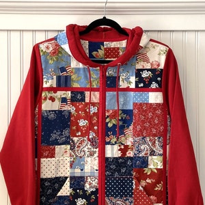 May include: Red hooded sweatshirt with a patchwork design featuring red, white, and blue fabric squares. The fabric squares have various patterns including floral, paisley, and polka dots.