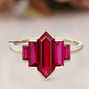 May include: A gold ring featuring a large, red, rectangular ruby gemstone in a geometric setting. The ruby is surrounded by three smaller, red, rectangular rubies.