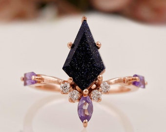 Puede incluir: Un anillo de oro rosa con una piedra preciosa azul oscuro en forma de cometa, rodeado de piedras preciosas más pequeñas transparentes y moradas.