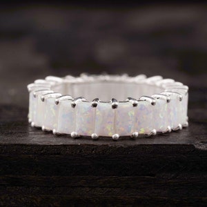 Puede incluir: Un anillo de banda de plata con una fila de piedras de ópalo blanco engastadas en forma rectangular.