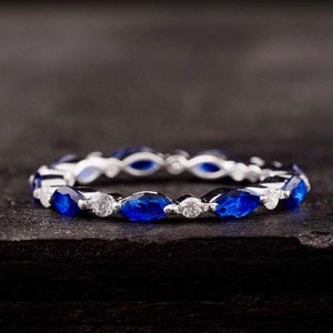 以下が含まれることがあります： 青色のマルキーズカットのサファイアと丸い白いダイヤモンドが交互に並んだシルバーのバンドリングです。