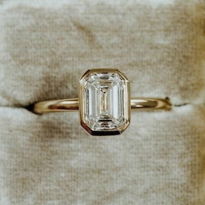 以下が含まれることがあります： 灰色のベルベットのリングボックスに入った、エメラルドカットのダイヤモンドがセットされた金のリング