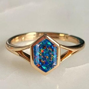 May include: A gold ring with a blue and orange opal gemstone set in a hexagonal bezel. The ring has a delicate, open band.