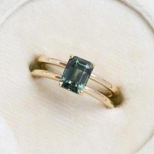 May include: A gold ring with a green emerald-cut gemstone set in a double band.