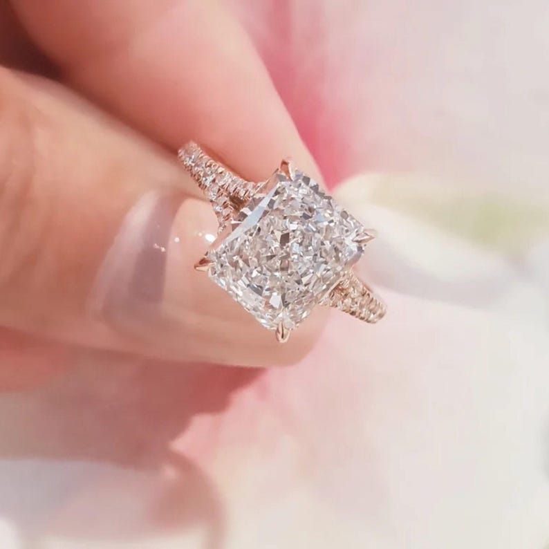 Puede incluir: Un anillo de compromiso de oro rosa con un gran diamante central de forma cuadrada y diamantes m&aacute;s peque&ntilde;os engastados en la banda.