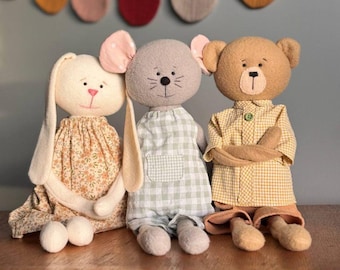 May include: Three handmade plush toys: a bunny wearing a floral dress, a mouse wearing a green and white gingham dress, and a bear wearing a yellow and white gingham shirt and pants.