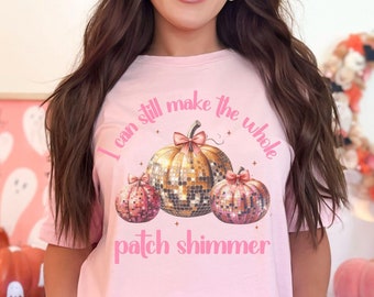 Op de afbeelding: Roze T-shirt met een afbeelding van drie glimmende pompoenen en de tekst "I can still make the whole patch shimmer".