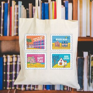May include: A white canvas tote bag with four colourful postage stamp designs. Each stamp features a house and text. The stamps read "People we meet on vacation", "Beach Read", "Happy Place", and "Book Lovers".