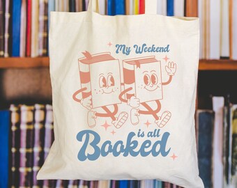 May include: A white canvas tote bag with a design of two cartoon books holding hands and the text "My Weekend is all Booked".