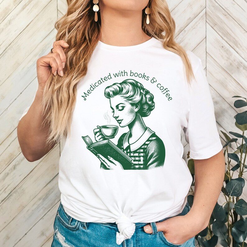 Op de afbeelding: Wit T-shirt met een groene illustratie van een vrouw die een boek leest en koffie drinkt. De tekst "Medicated with books & coffee" staat in een cirkel rond de illustratie.