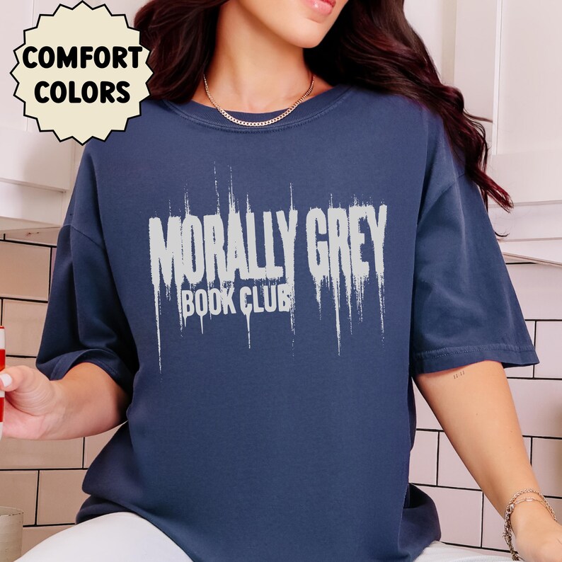 May include: Navy blue t-shirt with the text "MORALLY GREY BOOK CLUB" in a distressed white font. The shirt also has a "COMFORT COLORS" logo in a cream-colored circle.