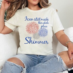 May include: A white t-shirt with a red, white, and blue firework graphic and the text "I can still make the whole place shimmer".